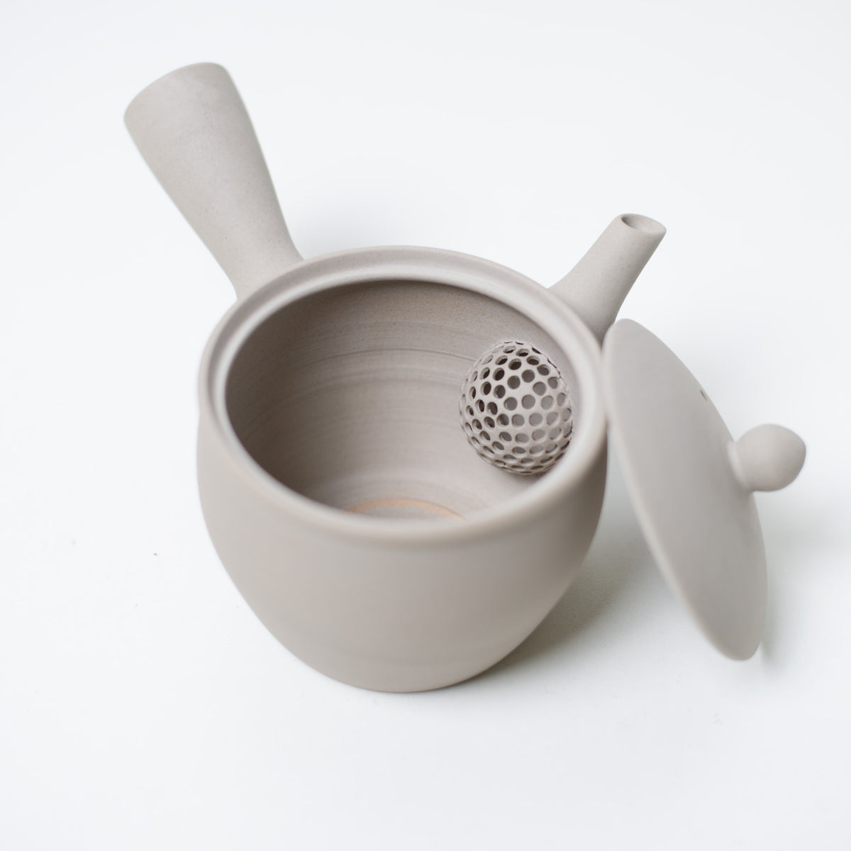 Open japanese teapot looking inside at the ceramic mesh strainer and lid of the white kyusu teapot