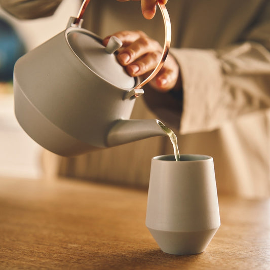 Hand pouring Japanese green tea from a modern Japanese teapot into a yunomi tea cup