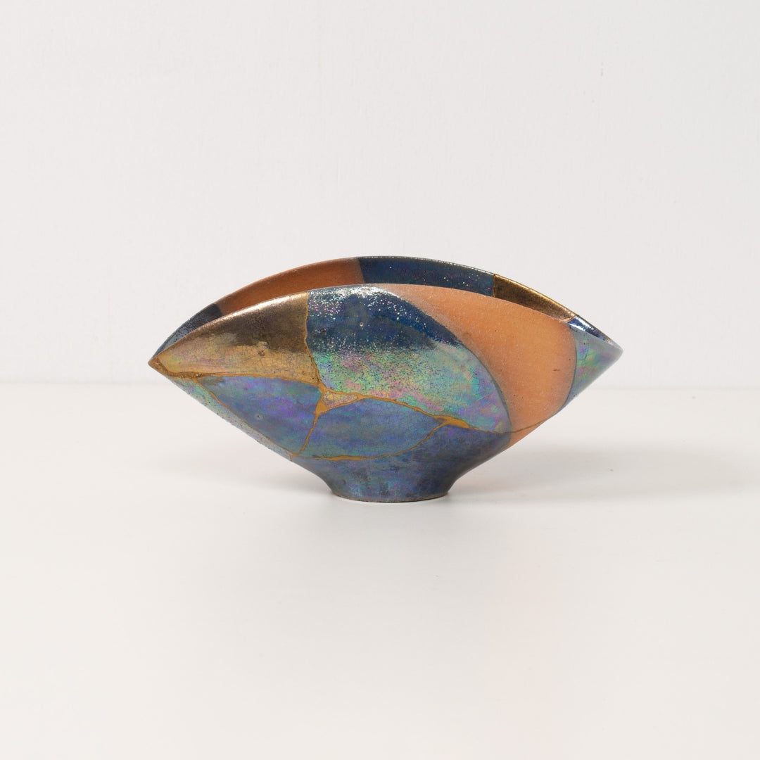 Un bol kintsugi asymétrique unique se dresse seul, mettant en valeur les glaçures colorées de la poterie kintsugi