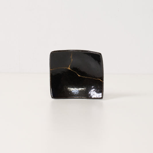 Close up of a black kintsugi plate revealing a bright golden lightning bolt repair symbolizing resilient pottery art