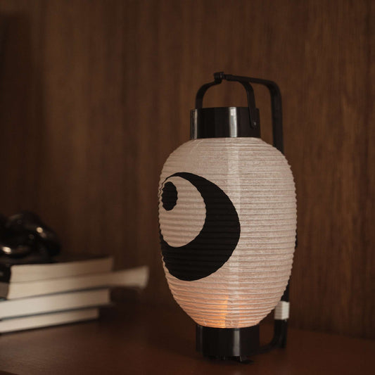 Lit Japanese paper lantern chochin on a dark wooden table displaying the traditional black ink design.