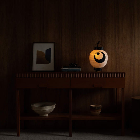Lit Japanese paper lantern standing on a mid century modern console table adding warm ambiance to a living room.