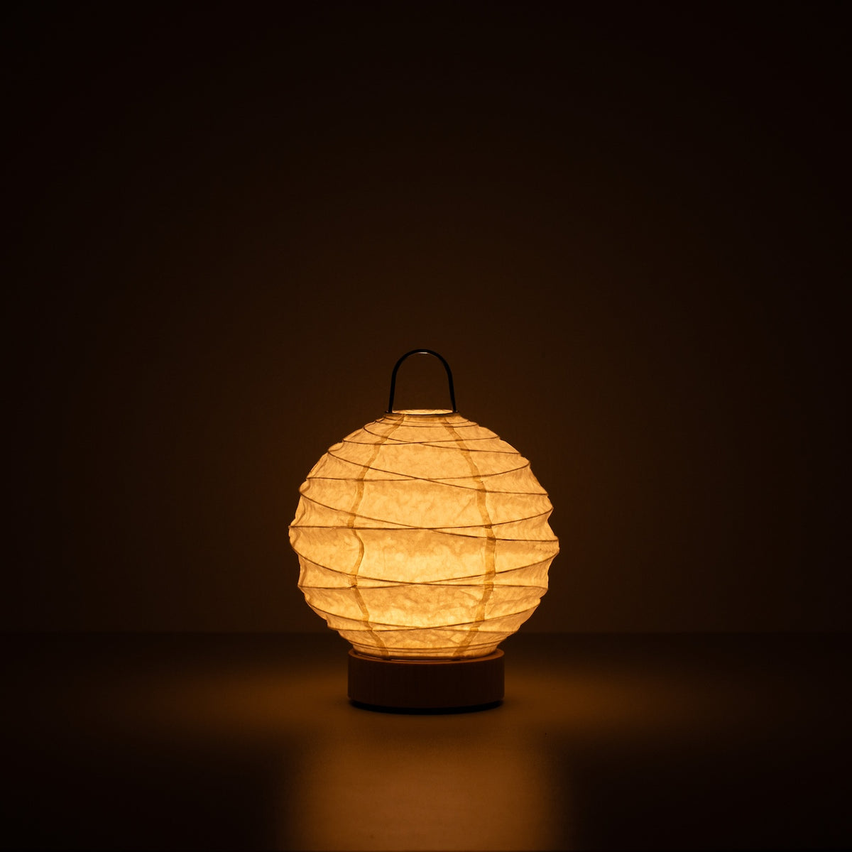 "Japanse Papieren Tafellamp \"Yuhi\", wit, Mino Washi papier - verlichte ronde papieren lamp die een warme gloed werpt in een donkere kamer."