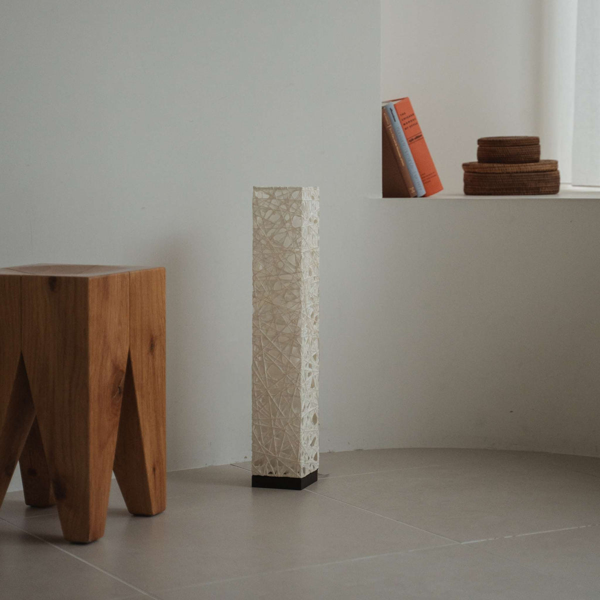 Compacte zwarte Me Look 02 papieren staande lamp, onverlicht op een betegelde vloer in een minimalistische witte kamer met boeken.