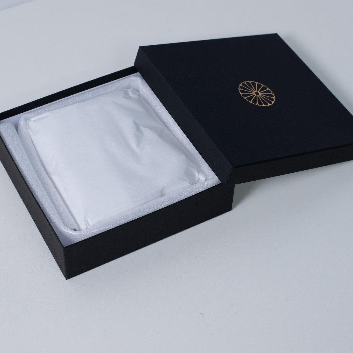 Open slim black Ninshu's gift box for Japanese incense holder pottery, showing a securely wrapped flat vessel inside white packaging paper.