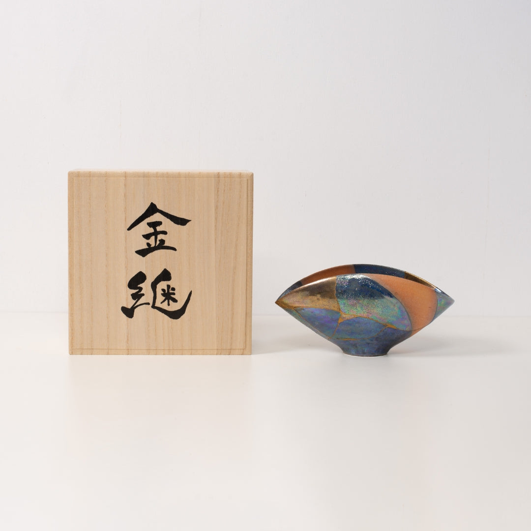 "Un bol kintsugi iridescent est posé à côté d'une boîte cadeau japonaise en bois présentant un art wabi sabi significatif"