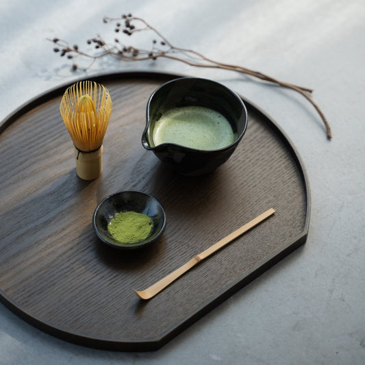 A Japanese matcha bowl with spout on a dark wood tray, part of a serene daily tea ceremony on a concrete table.