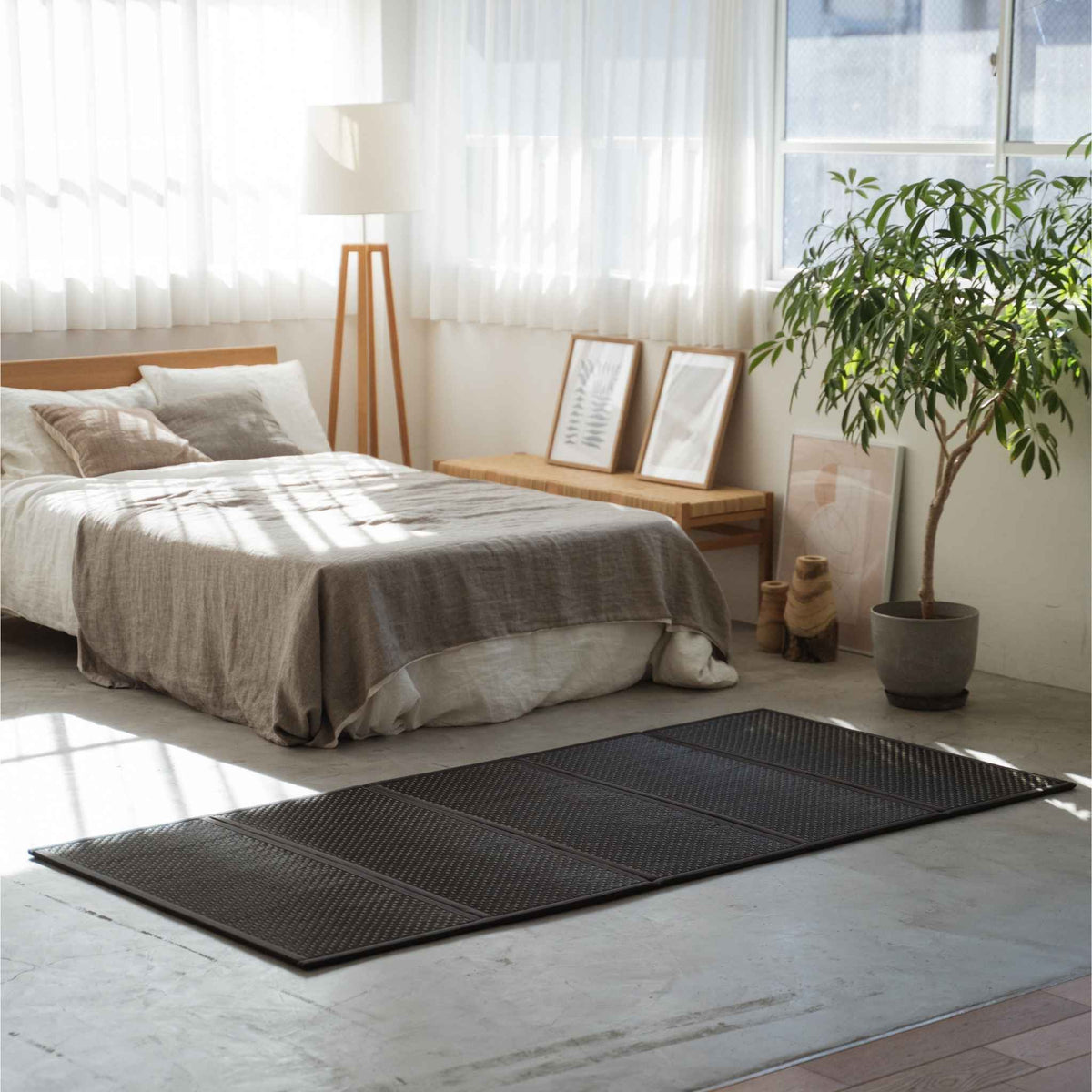 Enkele zwarte tatamimat op een betonnen vloer in een zonnige kamer met een minimalistische Japanse inrichting.