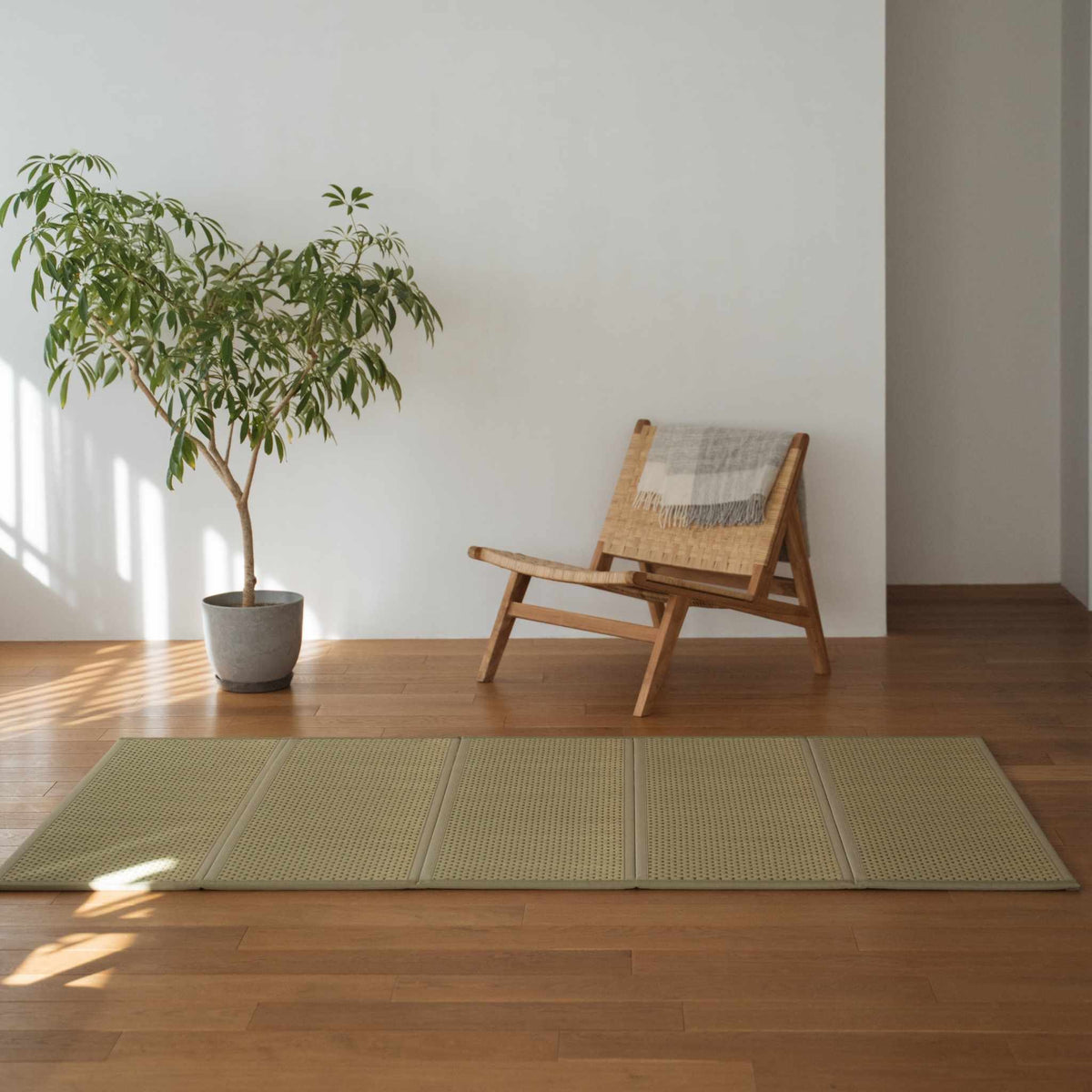 Groene dubbele tatamimat op een houten vloer naast een stoel en plant voor minimalistische Japanse decoratie.