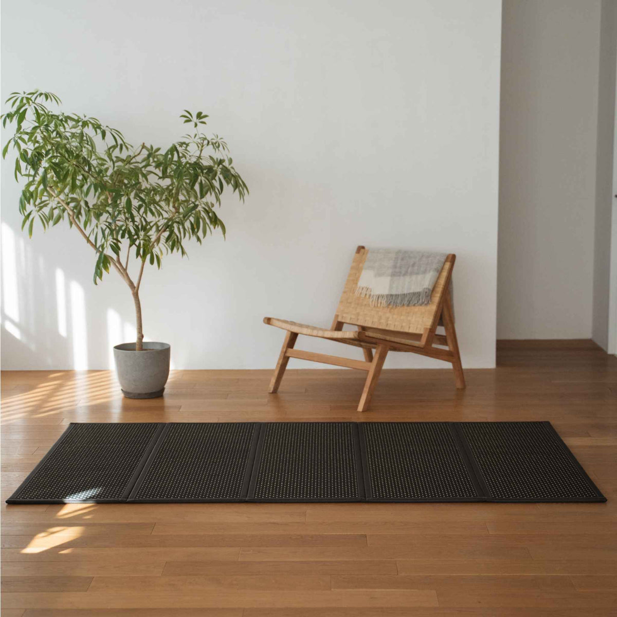 Zwarte tatami mat uitgevouwen op een houten woonkamervloer naast een stoel, dienstdoend als een moderne zen vloerkleed.
