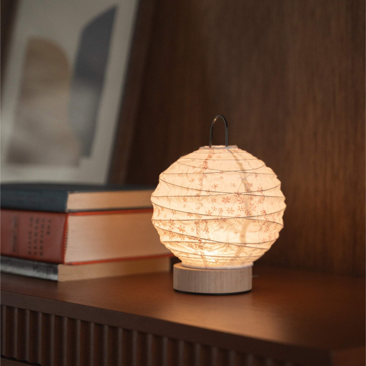 Japanse papieren tafellamp "Yuhi" Sakura die een warme gloed uitstraalt op een mid-century modern dressoir.