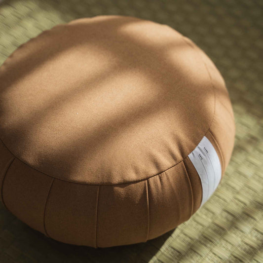 Close up detail of caramel brown zafu meditation cushion showing non slip suede like fabric texture on tatami.