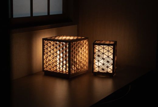 Two Kumiko Lanterns, each featuring a different intricate Japanese kumiko pattern, cast a warm glow in the corner of a traditional room.