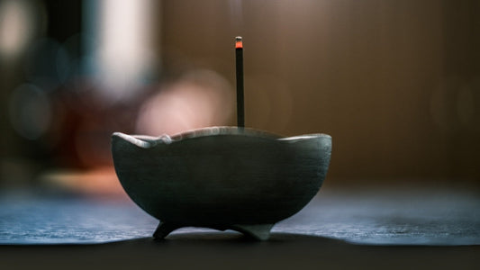 A close-up of a burning incense stick placed in a minimalist ceramic incense burner on a wooden surface