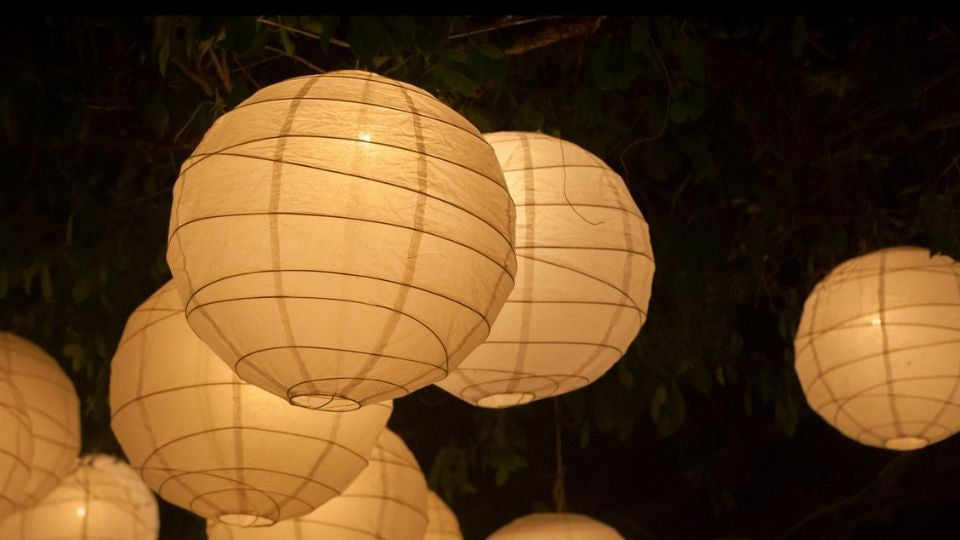 Outdoor Akari 37D Japanese paper lamp hanging among green leaves with a warm soft glow at night