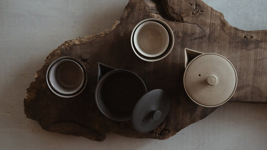 Overhead view of black and white Banko-yaki nested Japanese tea sets with handleless teapots and tea cups on a natural wood slab.