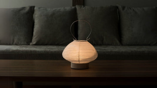 Japanse papieren tafellamp in lantaarnvorm die een warme gloed afgeeft op een houten tafel in een woonkamer