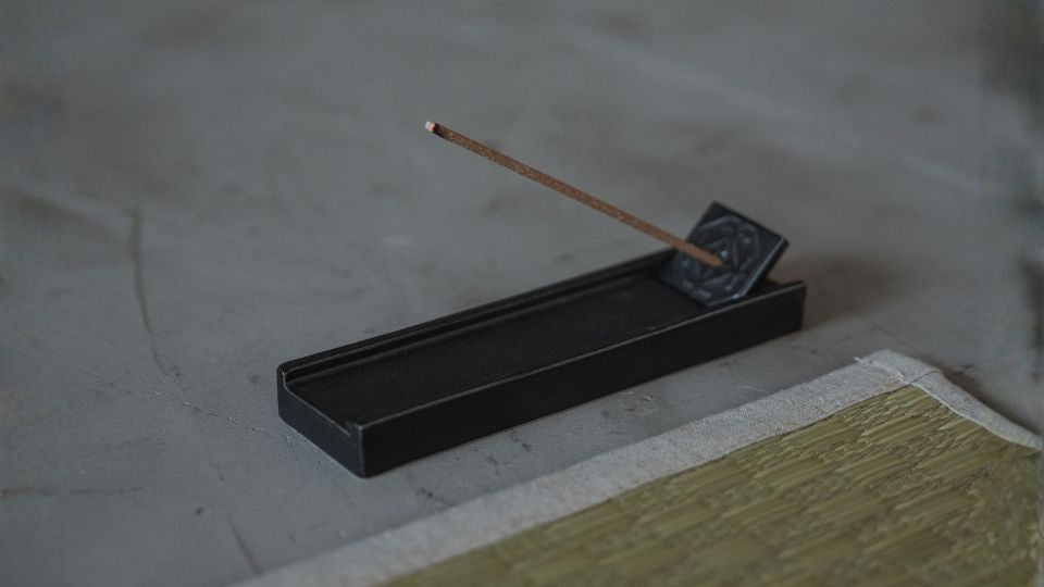 Un bâtonnet d'encens japonais brûlant repose dans un porte-encens japonais noir sur un sol à côté d'un tatami traditionnel.