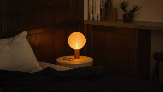 Warm washi japanese table lamp glows on a bedside table in a japandi bedroom, a portable lamp perfect for a japanese gift.