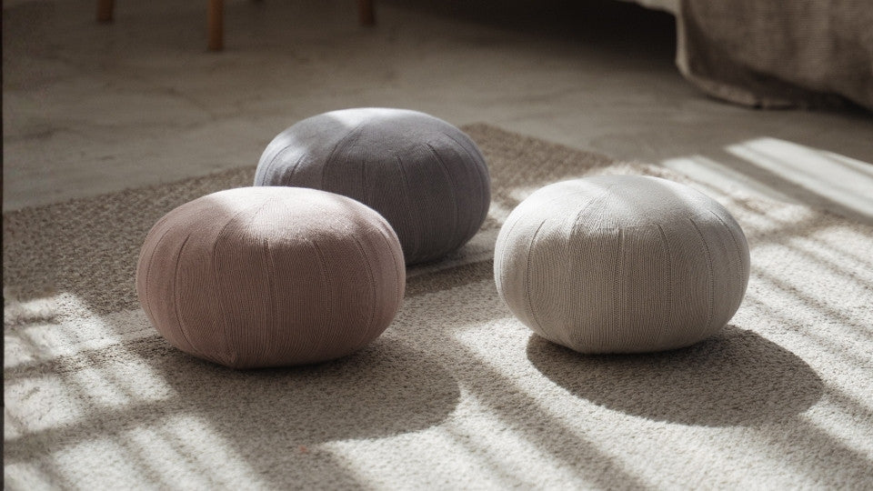 Three round zafu meditation cushions placed on the floor near a bed with linen sheets in a cozy room.