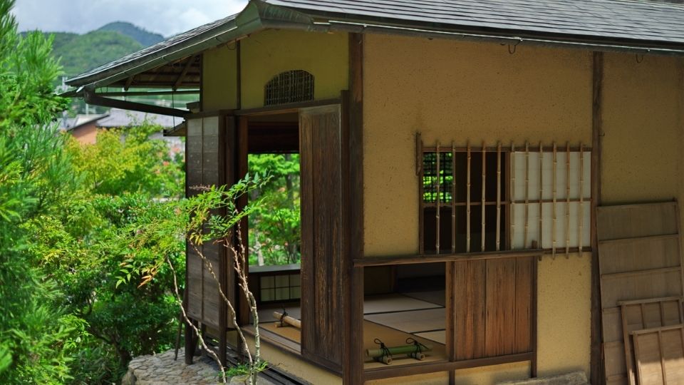 Traditionelles japanisches Teehaus Chashitsu mit offenen Holzläden und Tatami-Boden, umgeben von Gartengrün