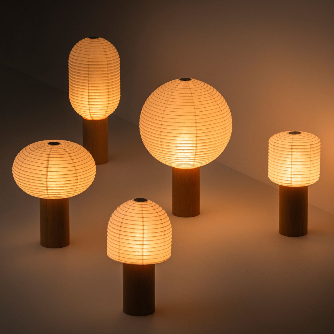 Five portable lamps, "TORCHIN", emitting a warm lamp, randomly arranged in a dimly lit room. The lampshades are made of Japanese washi paper from Yame-chochin lanterns, and each lamp has a wooden cylindrical handle.