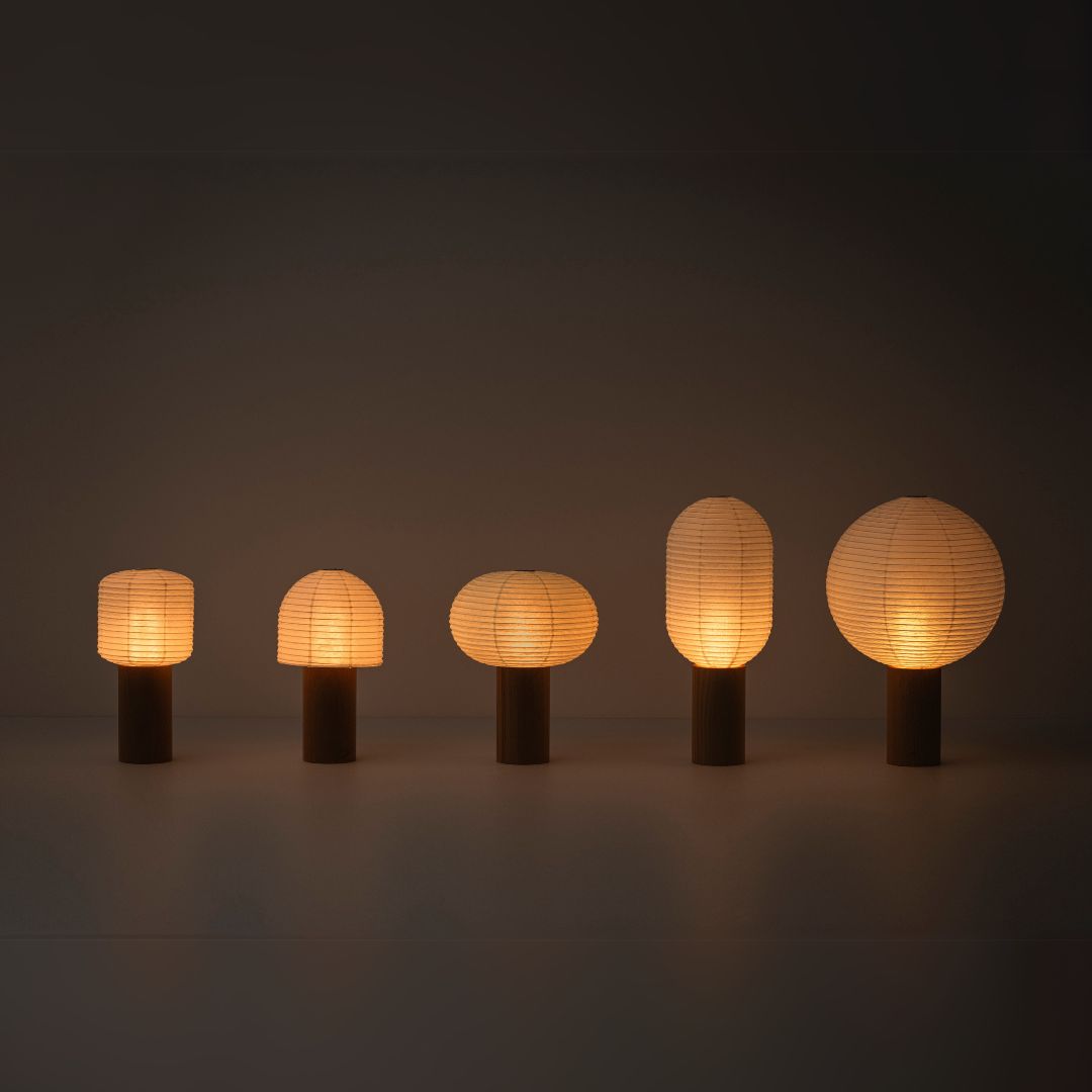 Five portable paper lamps, "TORCHIN", with warm lamp, lined up in a dimly lit room. The lampshades are made of Japanese washi paper from Yame-chochin lanterns, and each lamp has a wooden cylindrical handle.