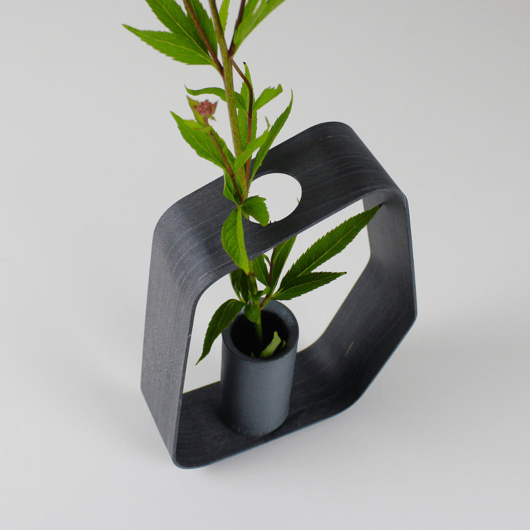 Close-up of a minimalist black iron vase crafted using traditional Japanese roof tile making techniques, paired with a black wood frame.