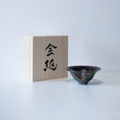 A bowl repaired using the challenging kintsugi technique of Kintsugi, where a piece of blown glass is attached, showcased in a paulownia wood box with the word "kintsugi" inscribed.