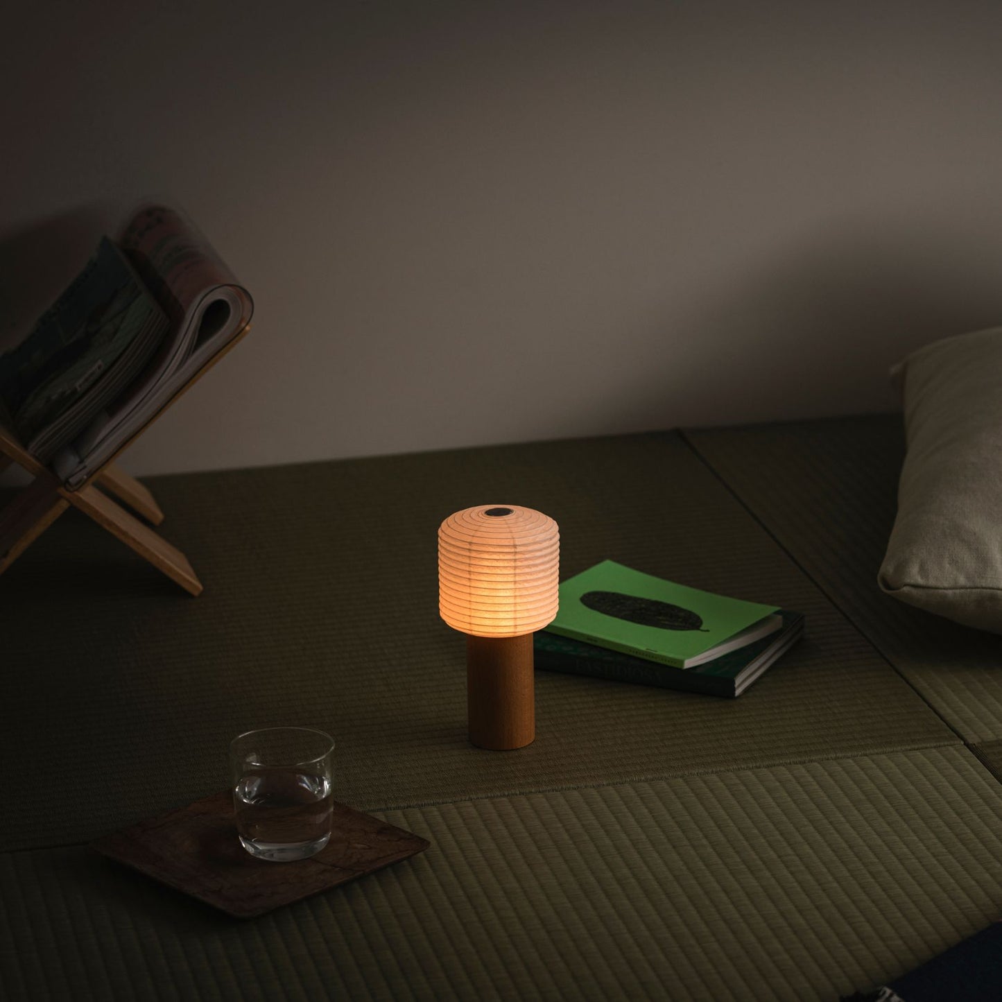 A portable paper table lamp glowing warmly, placed on a traditional Japanese tatami mat