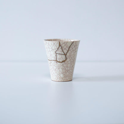 A white ceramic cup elegantly repaired using the kintsugi technique, showcasing the beauty of imperfection and the artistry of the repair.