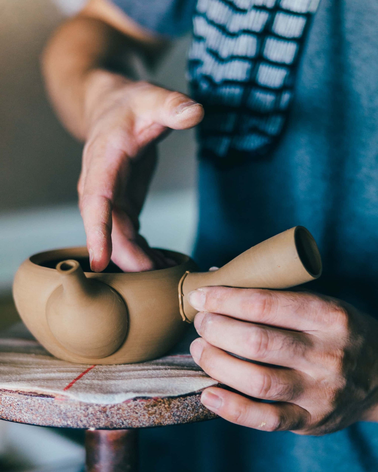 The artisan is shaping the teapot before firing it in the kiln.