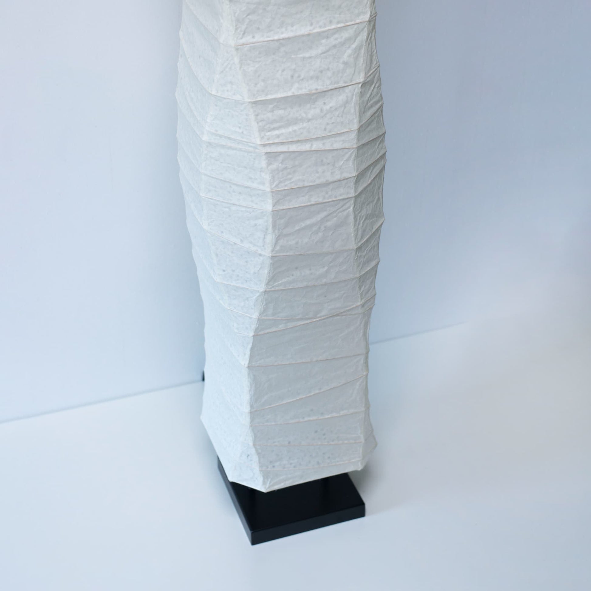 A close-up angled view of the lower part of a Japanese washi paper lamp, showing its smooth design on a white background