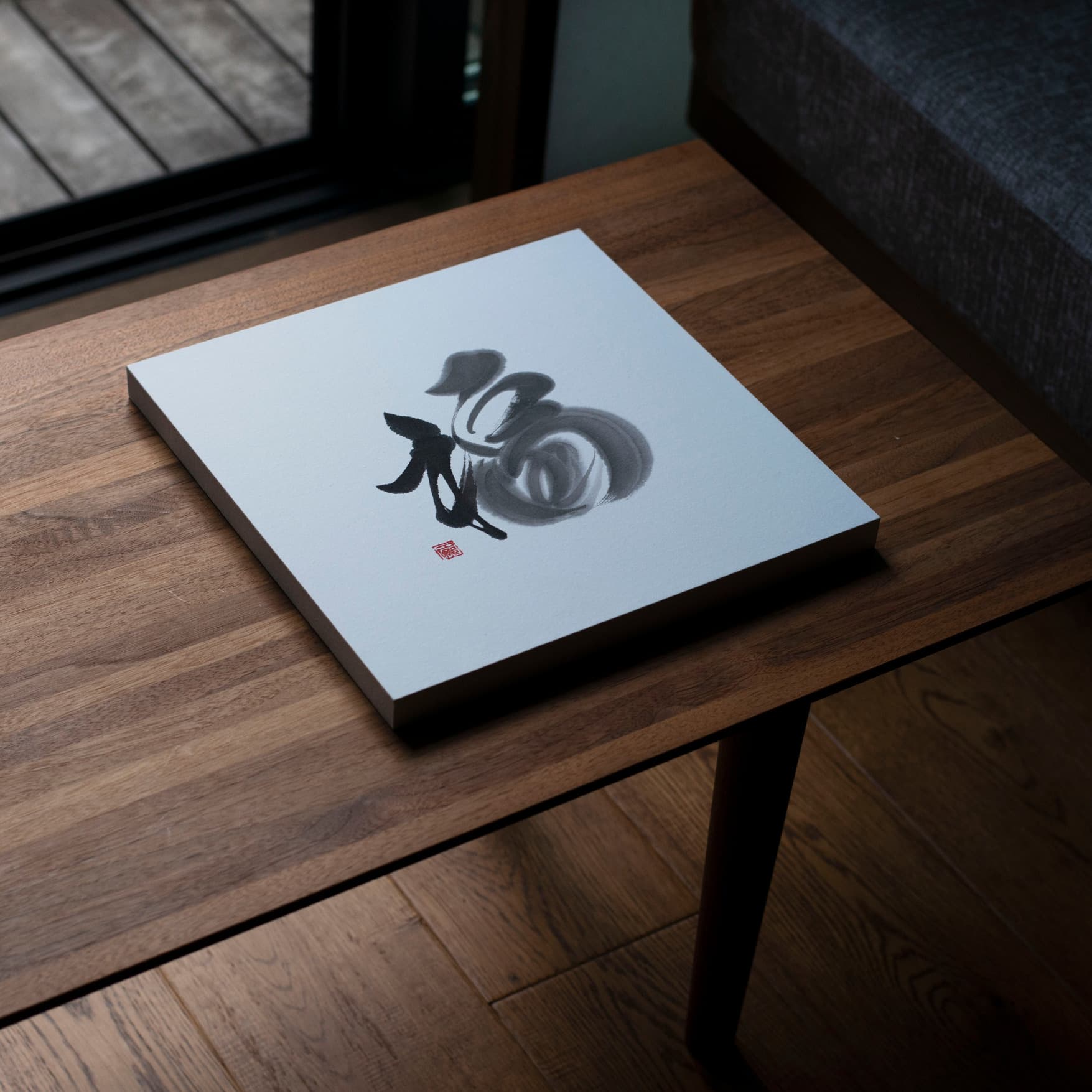 Angled top-down view of a square panel featuring the calligraphy of '福' (fortune), placed on a wooden table. 
