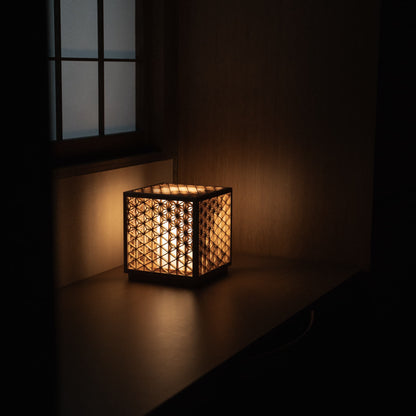 Kumiko lamp, meticulously handcrafted with 600 pieces of premium Akita cedar, casting a warm and inviting glow on a bedside table in a traditional Japanese bedroom.