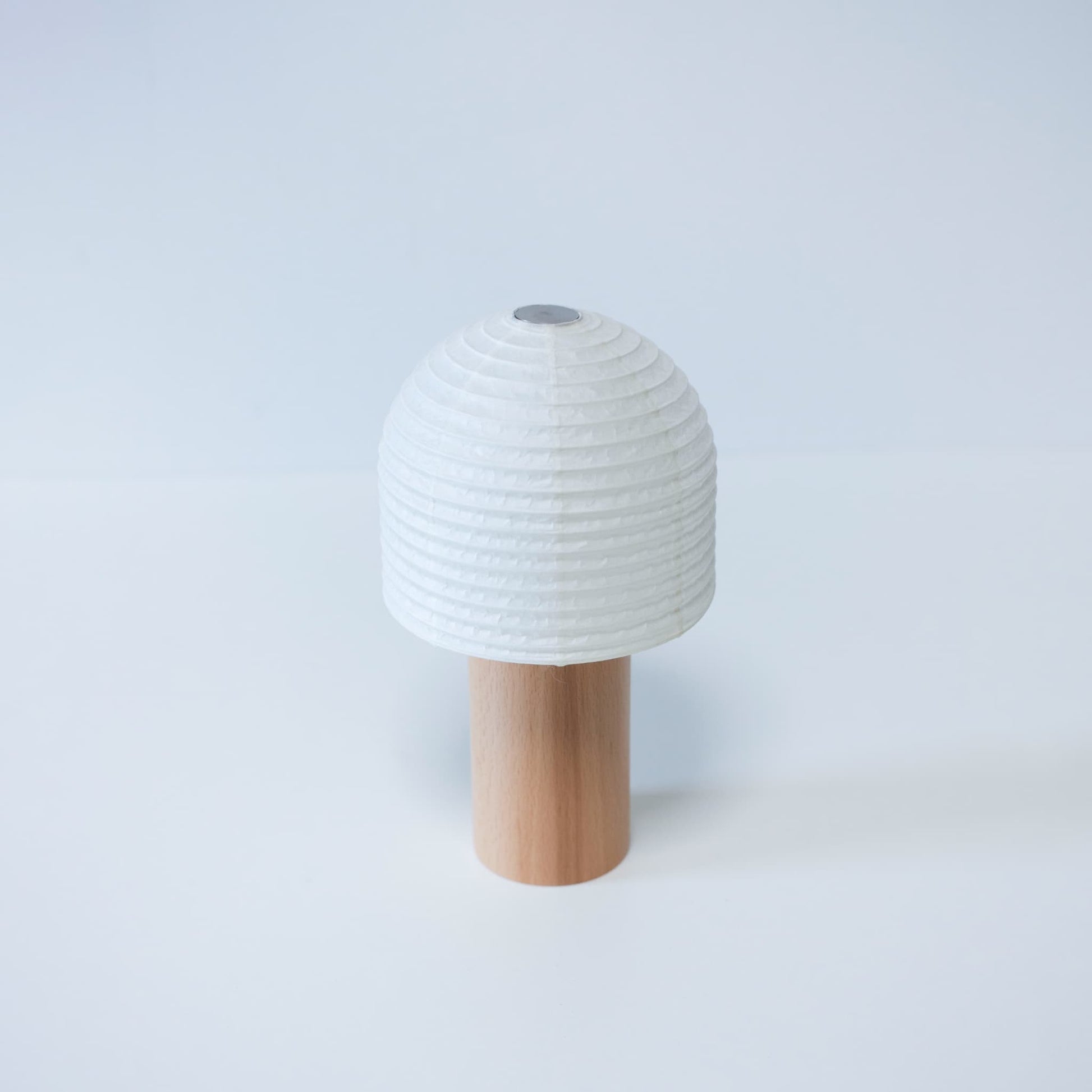 A portable Yame lantern with a bell-shaped paper top and wooden handle against a bright white background
