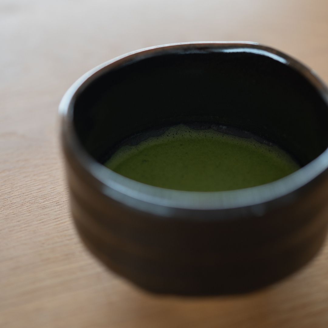 Close-up of vibrant emerald green matcha tea foam inside the deep black Japanese chawan bowl.