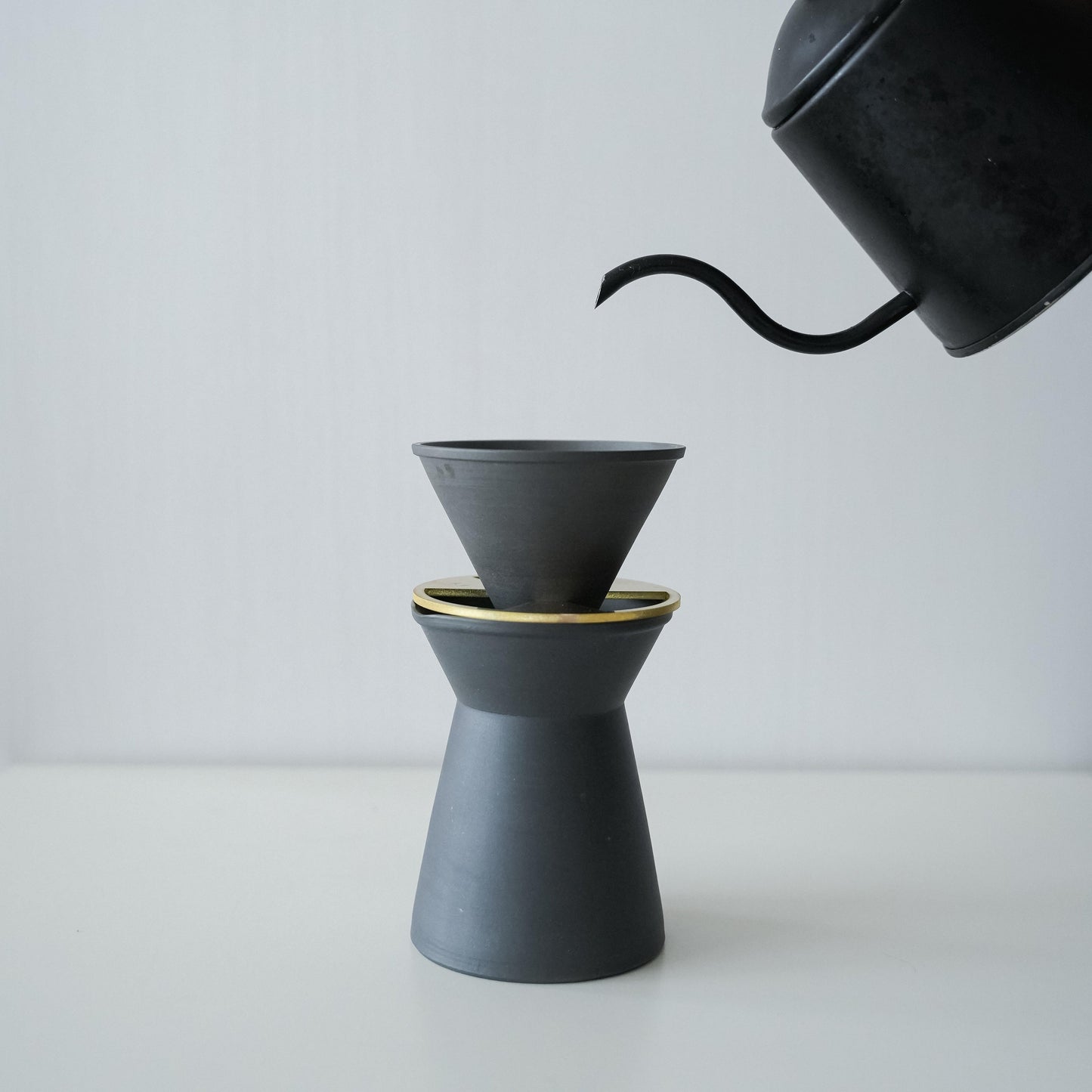 Pouring hot water from a black pot into a minimalist black Banko ware coffee server and dripper set.