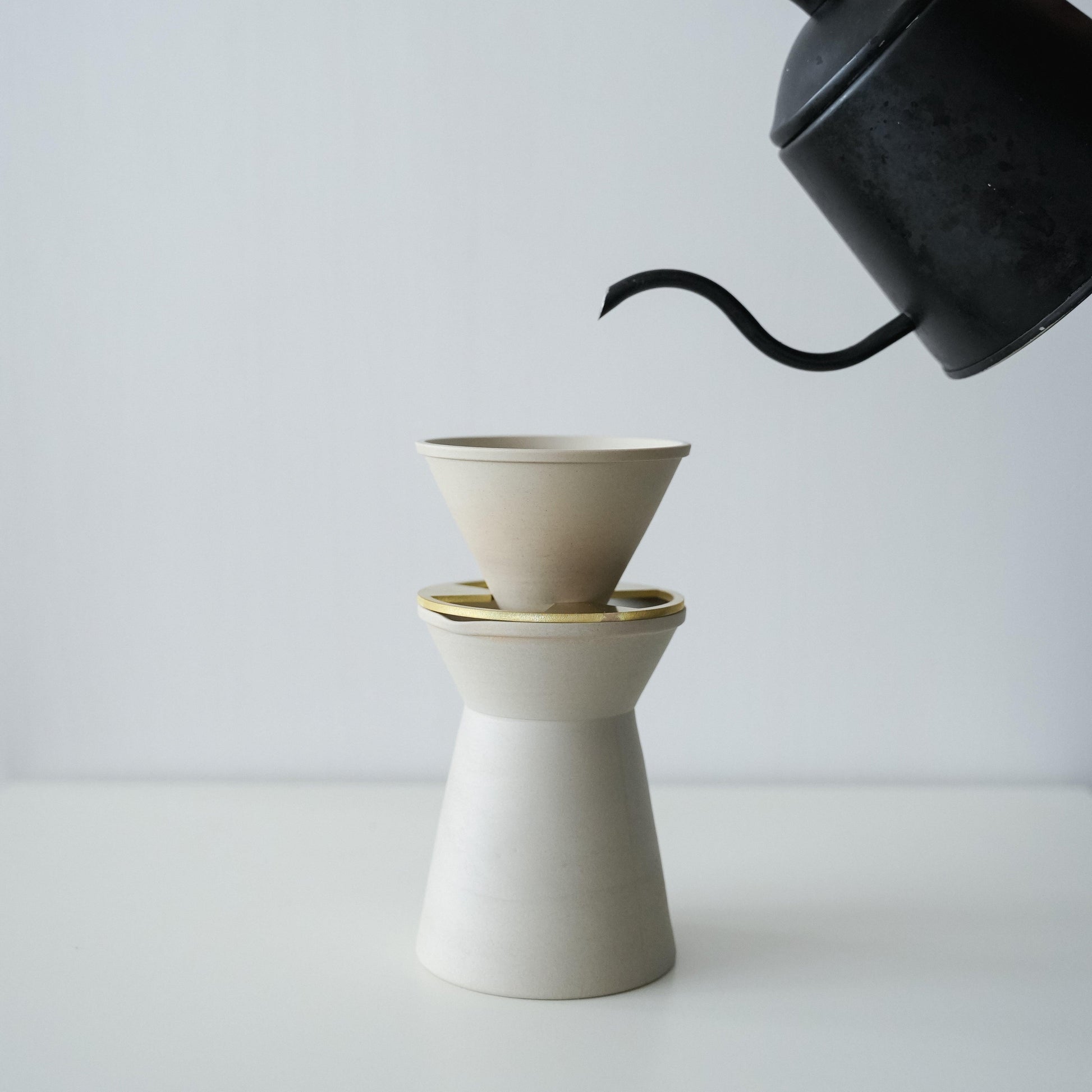 Pouring hot water from a black pot into a minimalist white Banko ware coffee server and dripper set.