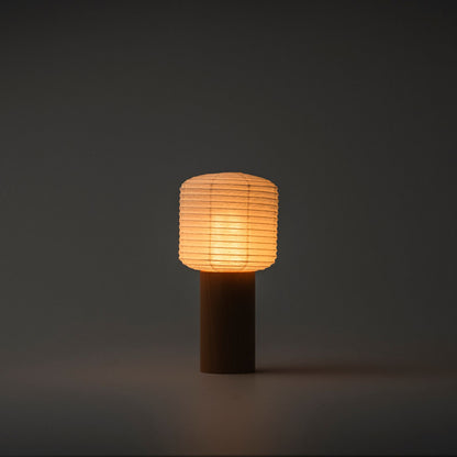 A portable Yame lantern brightly emitting warm light in a dark room, with a wooden handle and paper top