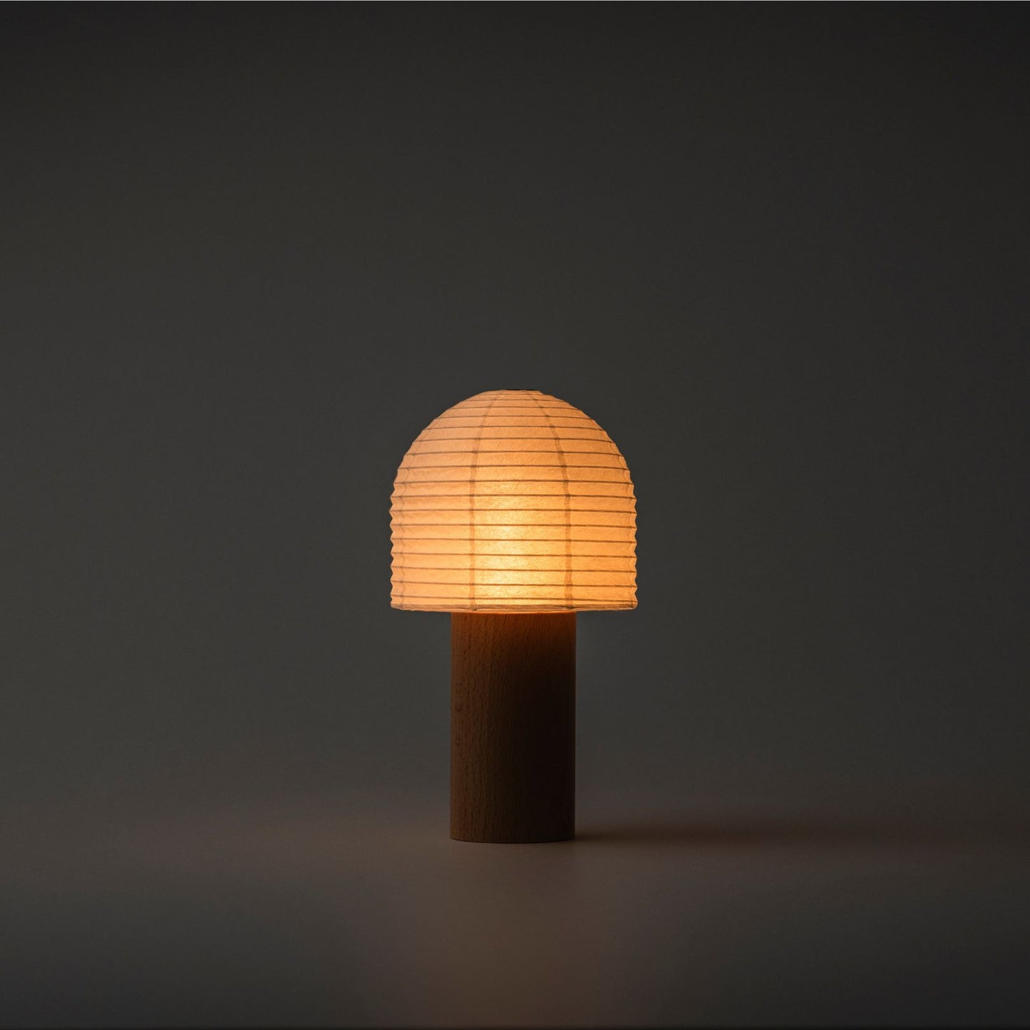 A brightly glowing Yame lantern with a bell-shaped paper top and wooden handle in a dark room