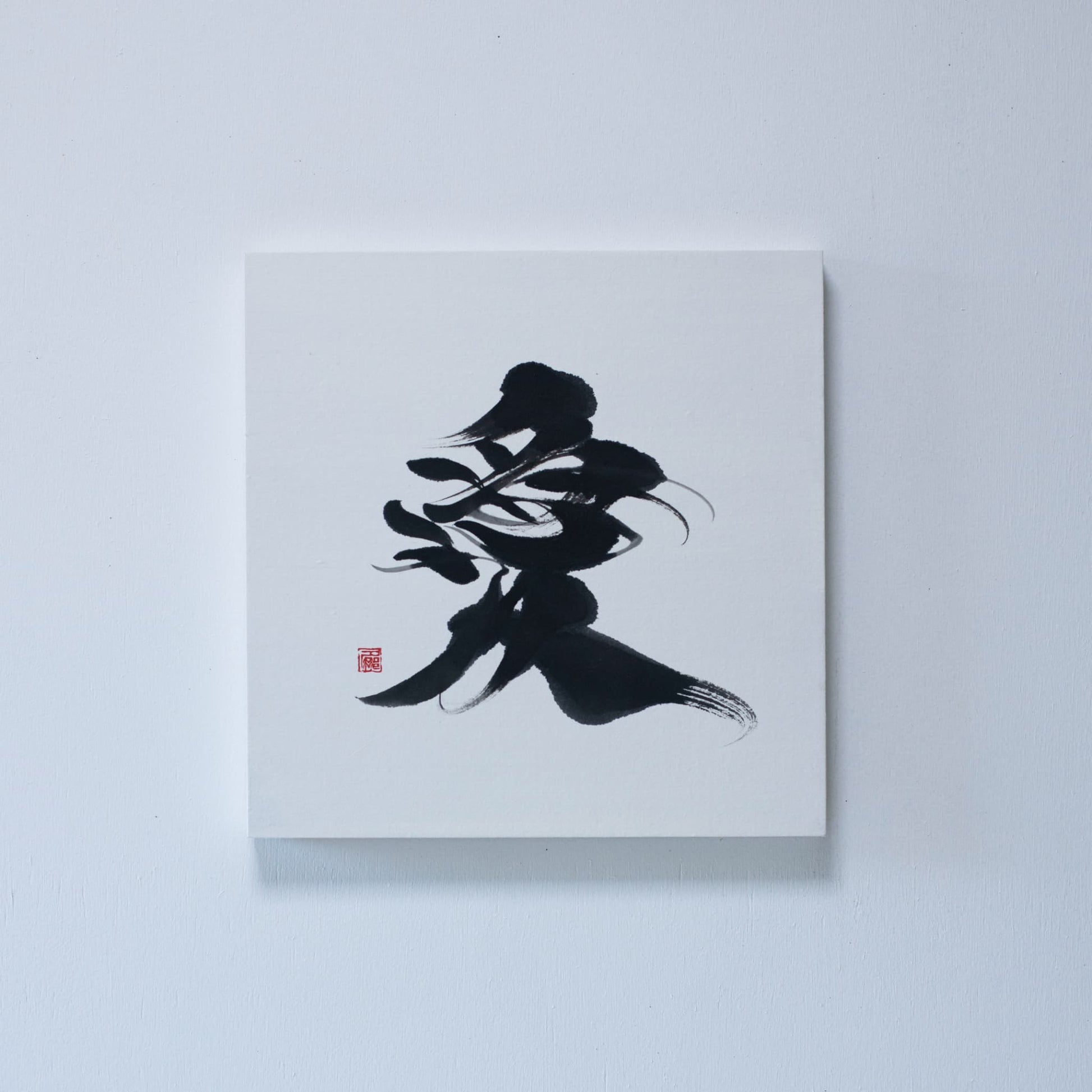 Square panel featuring Japanese calligraphy of the character '愛' (love) on white rice paper, mounted on a white wall