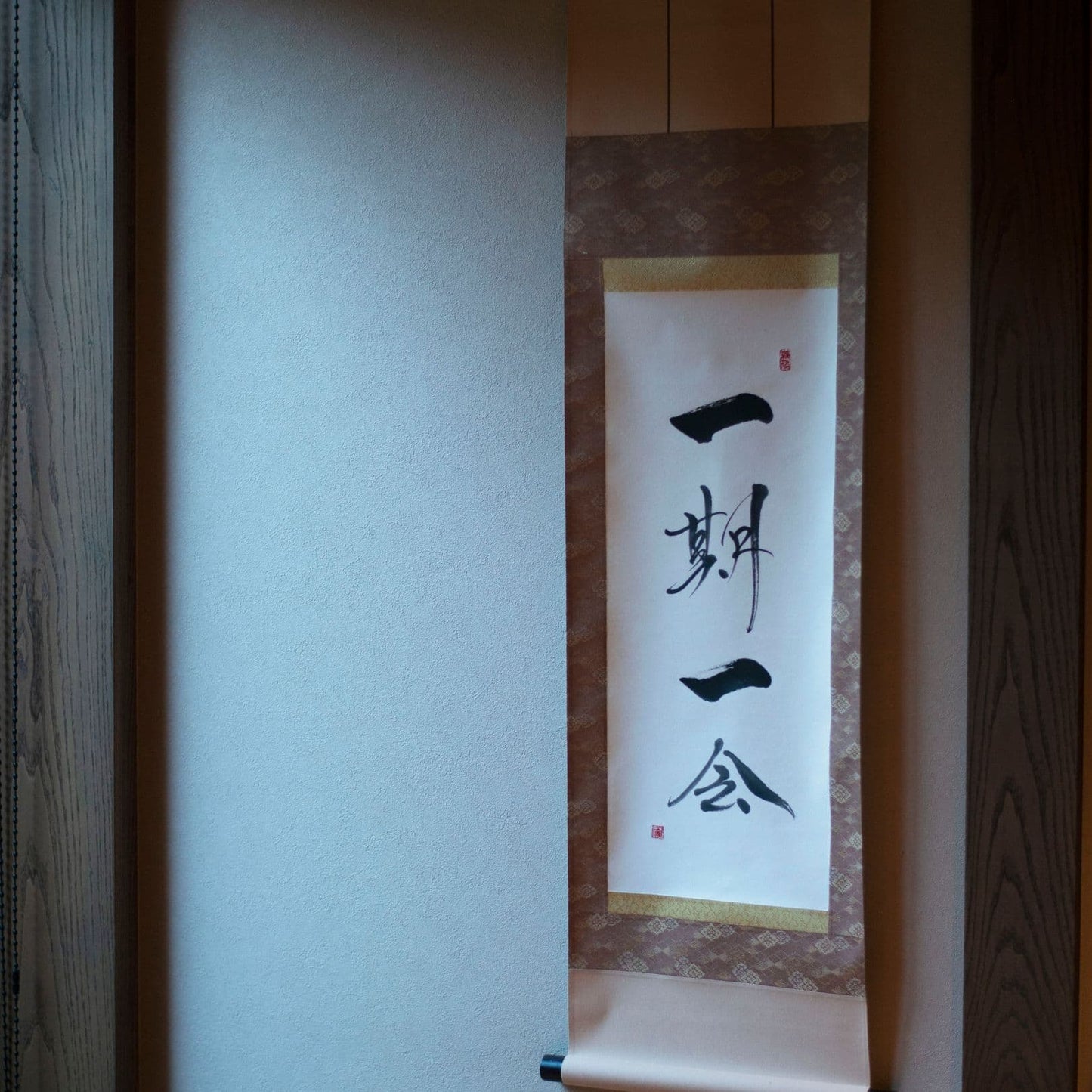 Side view of a traditional Japanese hanging scroll with '一期一会' (cherish every encounter) in calligraphy, displayed in a Japanese-style alcove