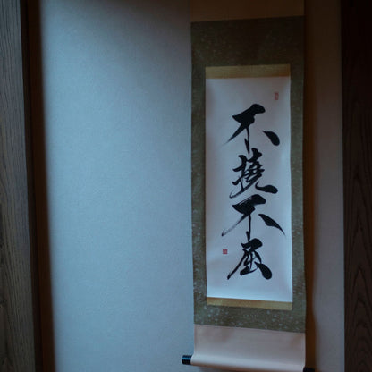 A side view of a hanging scroll in a Japanese-style alcove featuring the calligraphy '不撓不屈' (Unyielding Spirit)