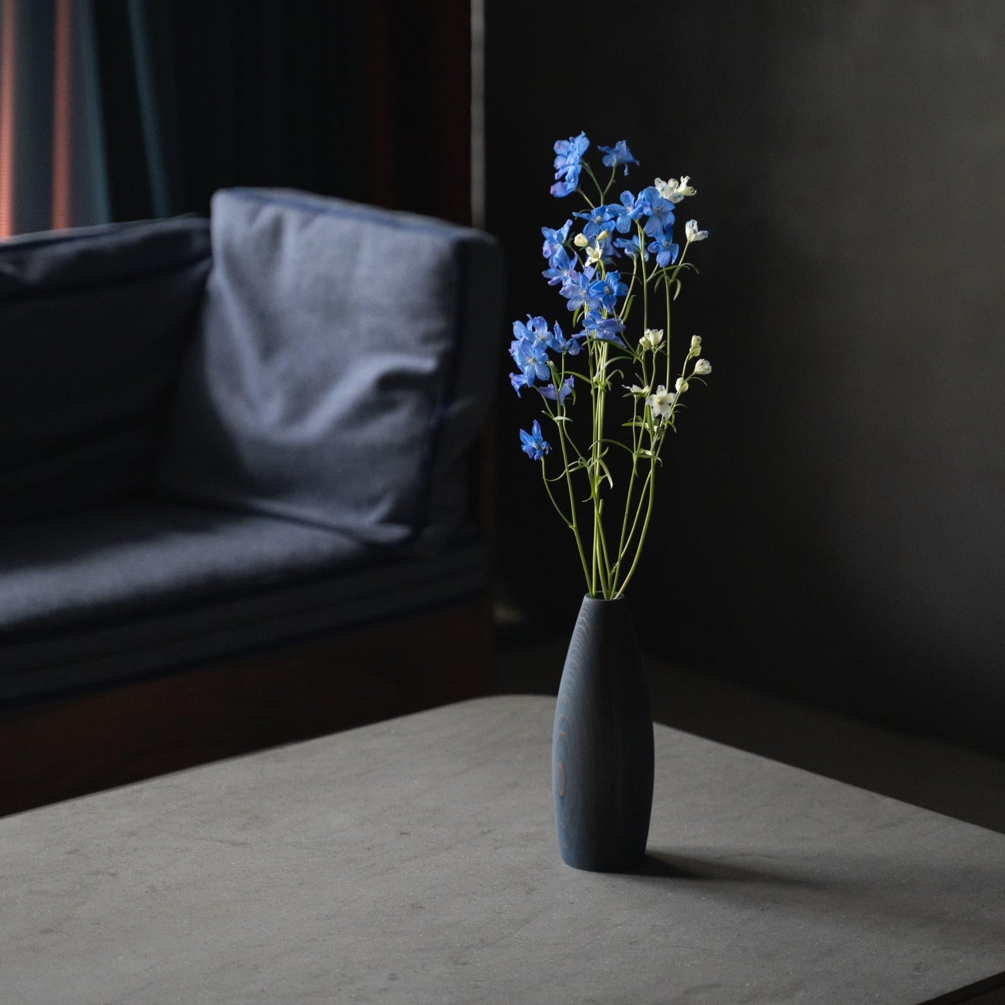 A beautiful cedar wood vase with blue flowers, adding a pop of color to a minimalist gray living room.