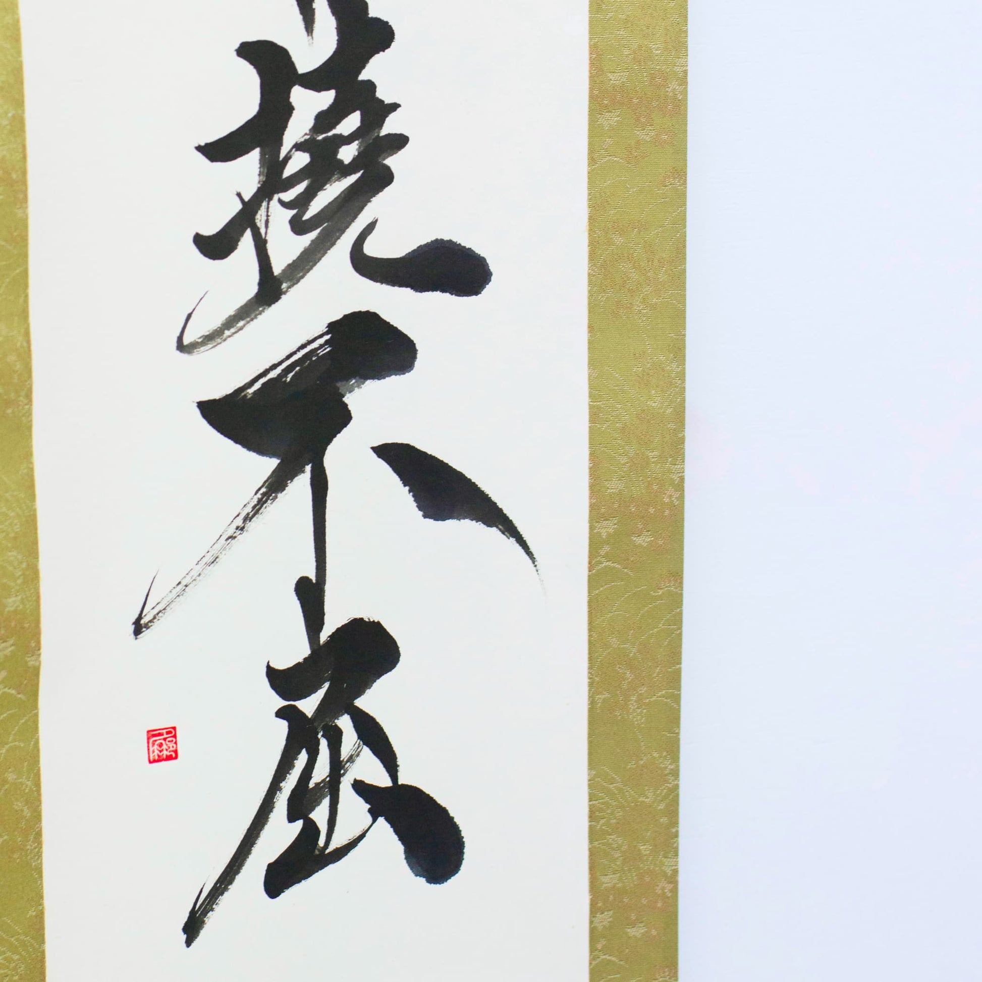 A close-up of the lower left corner of a traditional Japanese hanging scroll, showing the kanji '撓不屈' (Determined and Unyielding) in calligraphy