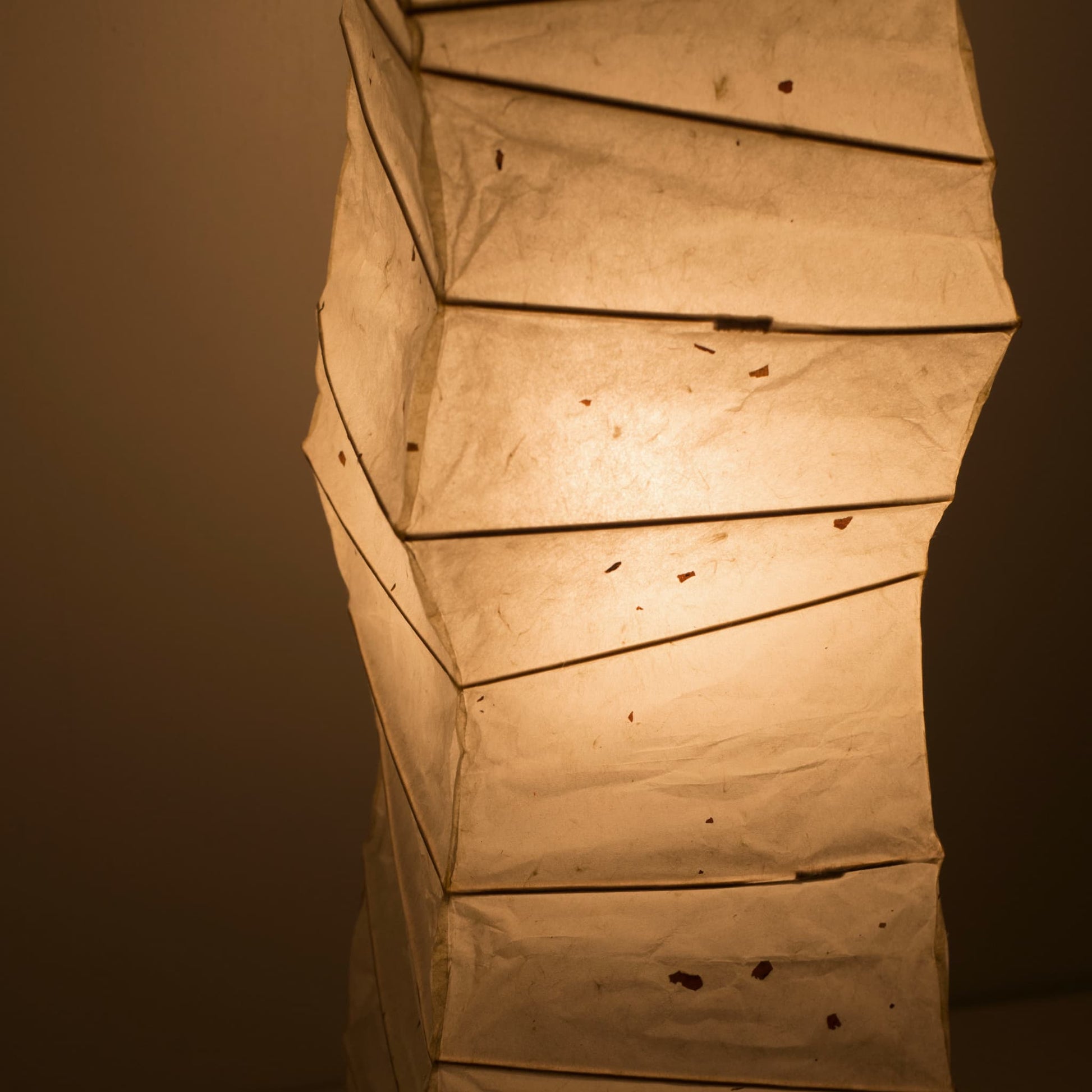 Angled top view of a curved Japanese washi paper lamp, highlighting the illuminated washi patterns on a brown background