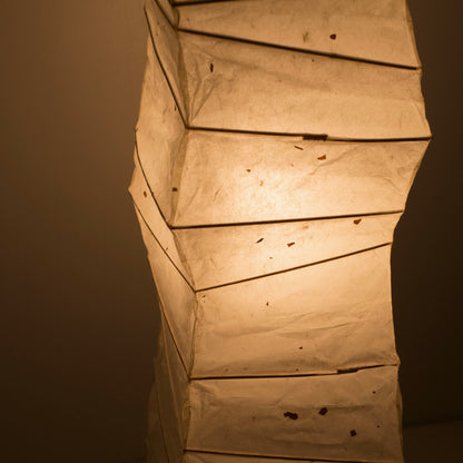 Angled top view of a curved Japanese washi paper lamp, highlighting the illuminated washi patterns on a brown background