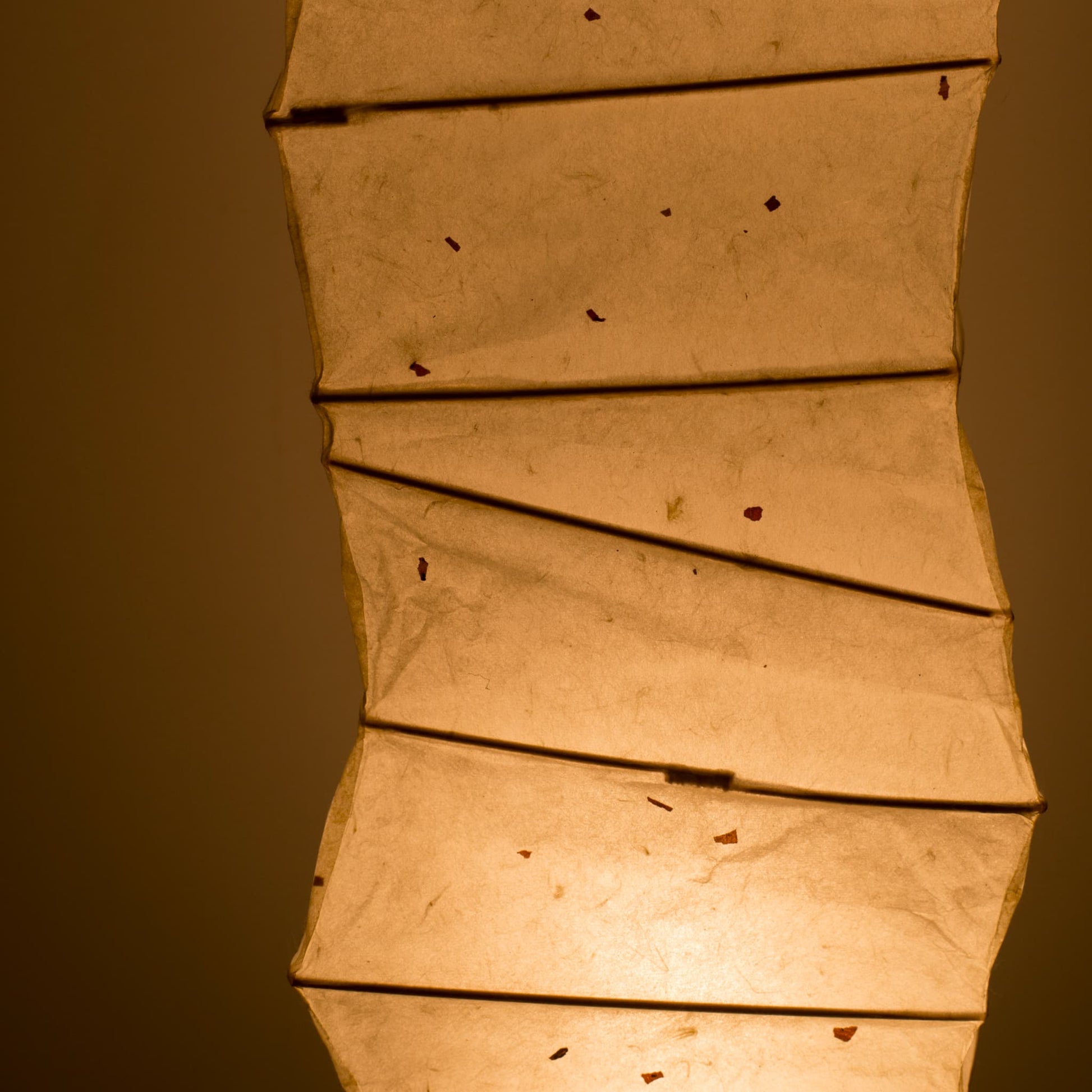 Detailed side view of a curved Japanese washi paper lamp, highlighting the illuminated washi patterns against a brown background