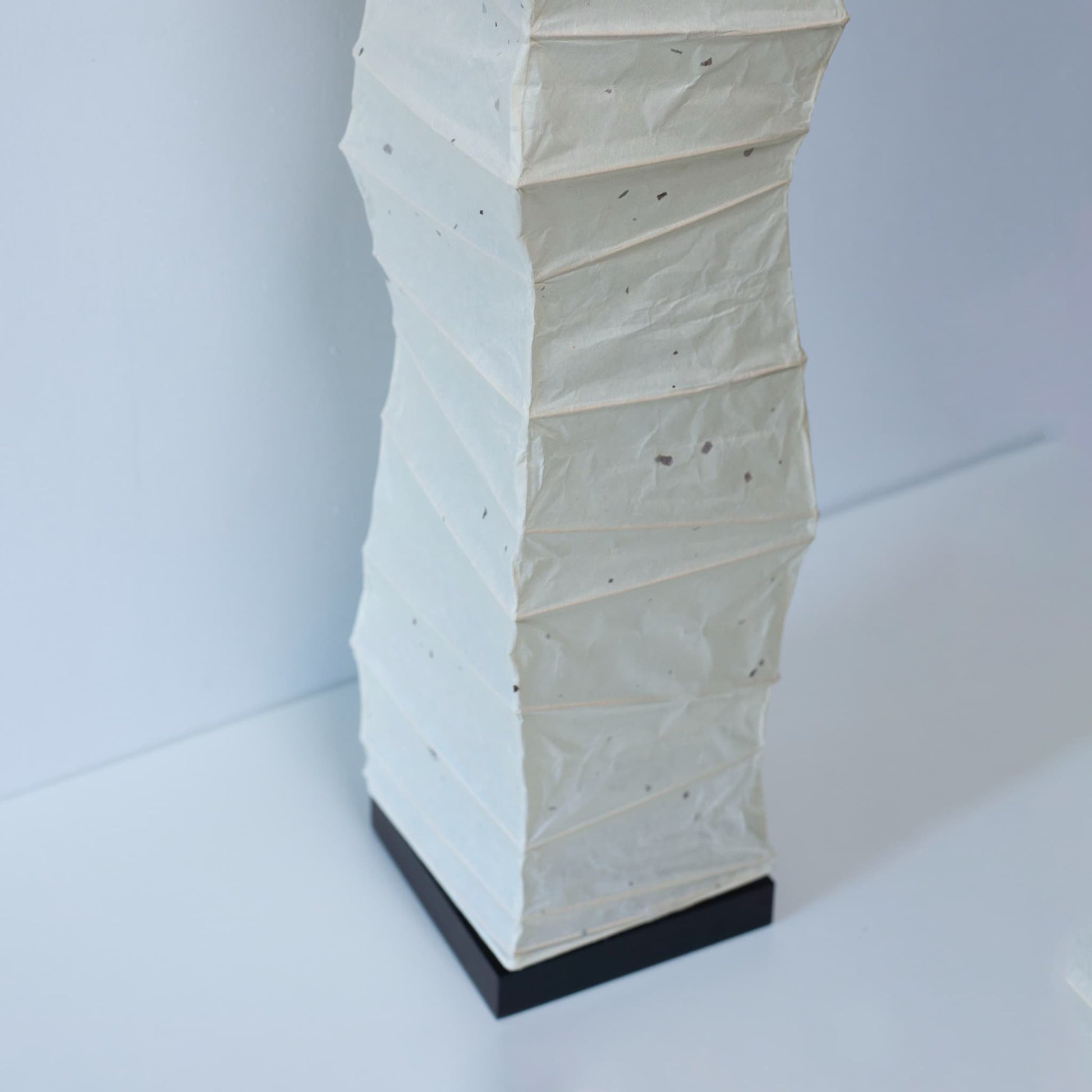 Close-up of the lower section of a curved Japanese washi paper lamp, shot from above on a white background